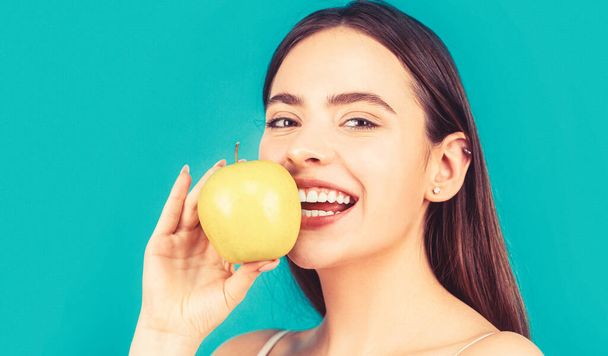 完璧な笑顔を保持リンゴ、青の背景を持つ女性。女性は緑のリンゴを食べる。緑のリンゴと若い美しい幸せな笑顔の女性の肖像画。健康的な食事. - 写真・画像