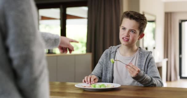 Chlapec, rodič a zelenina s rozčilenou tváří, frustrovaný a otrávený zdravým jídlem, jídlem a matkou doma. Matka, syn a dospívající nuceni jíst zeleninu, výživu a jíst na talíři u stolu doma. - Záběry, video