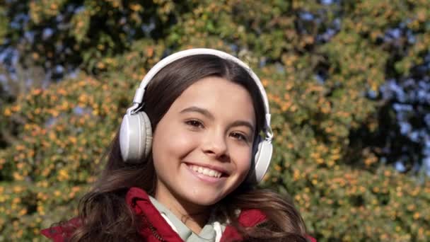 fröhliches Teenie-Mädchen mit Kopfhörern hört Musik. Kindheit von Teenagermädchen, die Musik über drahtlose Kopfhörer hören. Teenager-Mädchen hören Musik über Kopfhörer. Zeitlupe von Teenie-Mädchen hören Musik über Kopfhörer. - Filmmaterial, Video