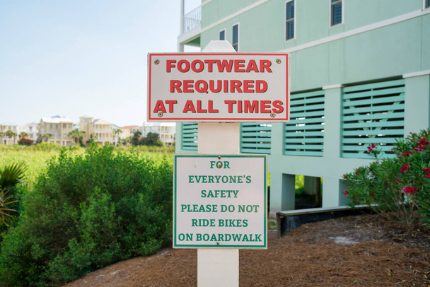 Írja alá a lábbelit Kötelező minden alkalommal, és kérjük, ne biciklizzen a sétányon a Destin, FL. Jelzőtábla kívül a világoszöld épület közelében a magas füvek a háttérben. - Fotó, kép
