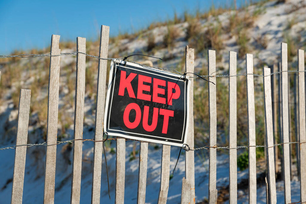 Destin, Florida- Manter fora sinal em uma cerca com madeira conectada por um fio de aço inoxidável. Assine em uma cerca contra uma areia inclinada com gramíneas na praia. - Foto, Imagem