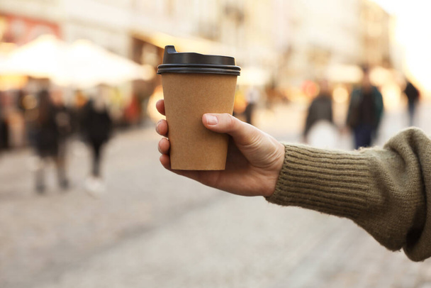 Woman holding paper takeaway cup on city street, closeup. Coffee to go - Zdjęcie, obraz