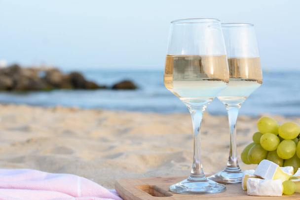 Glasses with white wine and snacks on sandy seashore. Space for text - Valokuva, kuva