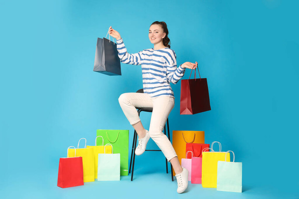 Happy woman holding colorful shopping bags on stool against light blue background - Foto, imagen