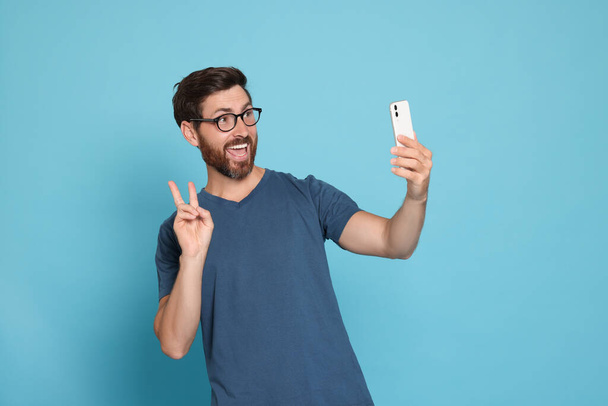 Happy man taking selfie with smartphone on light blue background - 写真・画像