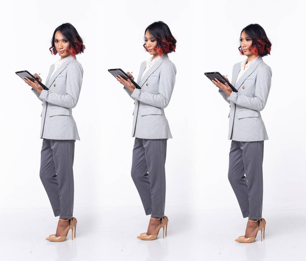 Full length 20s Ασιάτισσα γυναίκα φορούν επίσημη Business φόρεμα σακάκι ψηλά παπούτσια τακούνι. Μαύρο κοντά μαλλιά μπούκλα θηλυκό αισθάνονται ευτυχείς χαμόγελο κρατήσει δισκίο, 360 μπροστινή πλευρά πίσω πάνω από λευκό φόντο απομονωμένο - Φωτογραφία, εικόνα