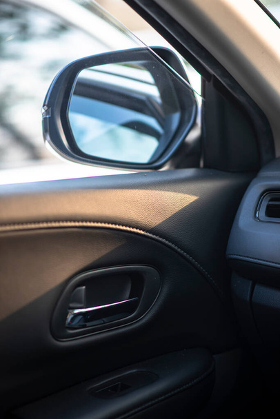 Folded wing mirror of a compact modern car, with a side window glass drop down for ventilation, seeing an inner car door handle. Car parked in a parking lot during the morning time with sun rise. - Foto, Imagen
