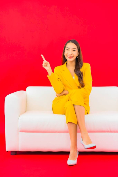Muotokuva kaunis nuori aasialainen nainen istuu sohvalla tuoli punaisella taustalla - Valokuva, kuva
