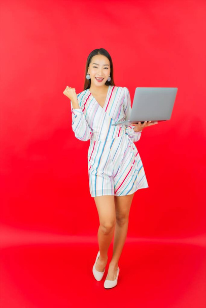 Güzel bir Asyalı kadının portresi kırmızı arkaplan üzerinde çalışmak için bilgisayar bilgisayarı kullanıyor. - Fotoğraf, Görsel