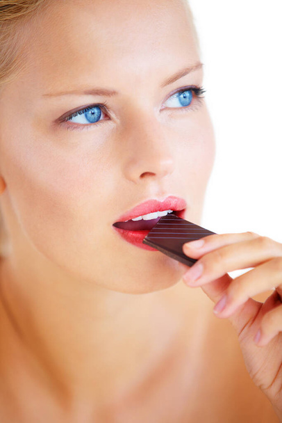 Chocolate is filled with antioxidants. Beautiful young woman enjoying a delicious piece of chocolate - 写真・画像