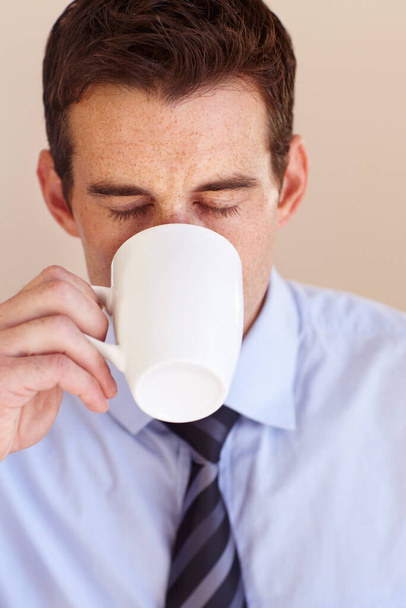 Er kann nicht mit dieser ersten Tasse Kaffee zur Arbeit gehen... Junger Geschäftsmann nippt an einer Tasse Kaffee - Foto, Bild