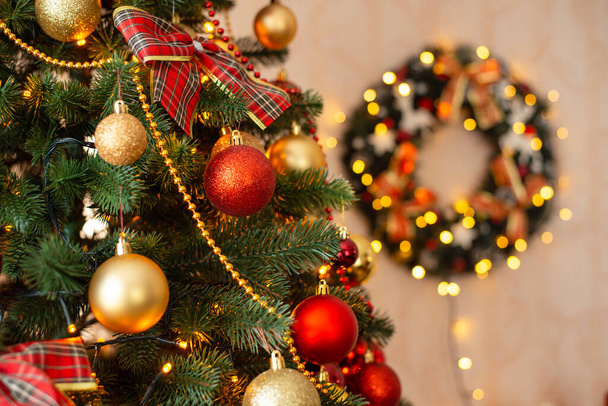 Közelkép a karácsonyfáról. Karácsonyfa díszített baubles, fények az előtérben, koszorú a háttérben. - Fotó, kép