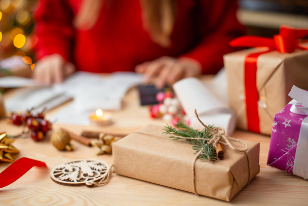 Nahaufnahme des handgemachten Geschenks auf dem Hintergrund des Mädchens, das überprüft, ob alle Geschenke bereit sind, sich darauf vorbereiten, sie Freunden und Verwandten zu schicken. Vorbereitungen für Weihnachtsgeschenke - Foto, Bild