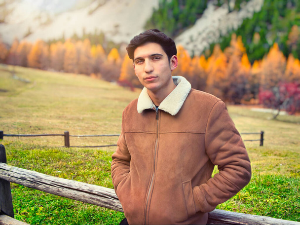 Attractive young man in the mountains in autumn or winter, cold weather, wearing suede jacket, looking at camera - Fotoğraf, Görsel