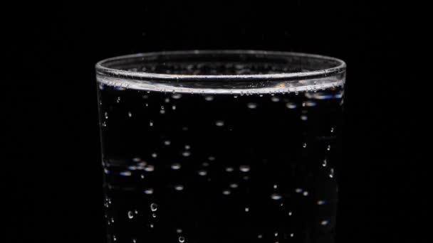 Szklankę wody gazowanej na czarnym tle. Bąbelki wychodzą ze szkła. Czysta woda mineralizowana z gazem. - Materiał filmowy, wideo