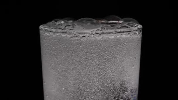 A glass of sparkling water on a black background. Bubbles come out of the glass. Pure mineralized water with gas. - Footage, Video