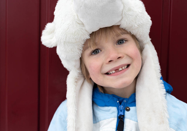 Sıcak kürk şapkalı, soğuk kış mevsiminde samimi dişsiz gülümsemesi olan anaokulu çocuğunun sevimli portresi. Bir dişin düştüğüne sevinmelisin. Diş perisini bekle. - Fotoğraf, Görsel
