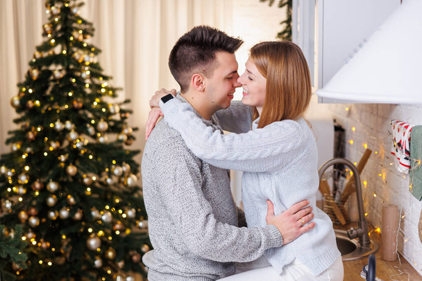 Ευτυχισμένο νεαρό ζευγάρι που αγκαλιάζεται στην κουζίνα διακοσμημένο για το νέο έτος. Το εσωτερικό της Πρωτοχρονιάς στην κουζίνα. Χριστουγεννιάτικη κουζίνα - Φωτογραφία, εικόνα