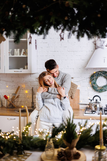 Happy young couple hugging in the kitchen decorated for the new year. New Year's interior in the kitchen. Christmas kitchen - Фото, изображение