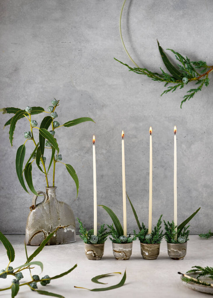 4. Advent. Christmas decor with white narrow candles, eucalyptus leaves and fruits in four ceramic mugs. Handmade home decoration. Selective focus. Copy space.(Eucalyptus globulus) - Foto, afbeelding
