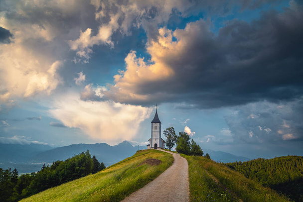 Vidéki táj kis templommal a hegygerincen. Felhős táj és aranyos alpesi Szent Primoz templom naplementekor, Jamnik falu, Szlovénia, Európa - Fotó, kép