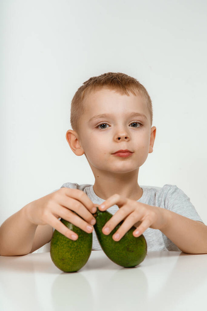 Healthy food and vegetarianism. Boy Showing Avocado and Thumb Up Close Up Isolated. Avocado Cut in Half. Little kid with fresh avocado on light background. High quality photo. - Fotó, kép