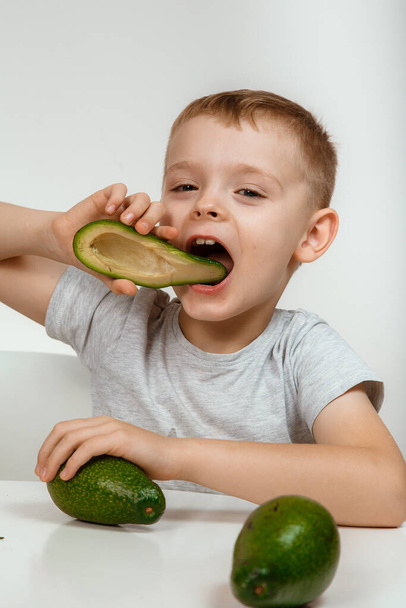 Healthy food and vegetarianism. Boy Showing Avocado and Thumb Up Close Up Isolated. Avocado Cut in Half. Little kid with fresh avocado on light background. High quality photo. - Фото, изображение