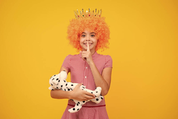 Teenager princess child in fancy clown wig hug toy. Teen girl in queen crown isolated on yellow background - Photo, Image