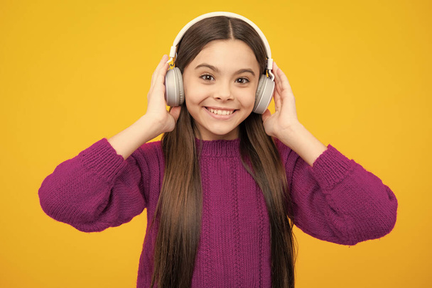 Teen girl in headphones listen to music. Wireless headset device accessory. Child enjoys the music in earphones on yellow background - Photo, image