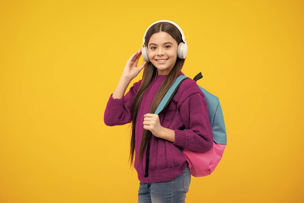 Back to school. Schoolgirl student in headphones with school bag backpack on isolated studio background. School and education concept. Teenager girl in school uniform - Fotoğraf, Görsel