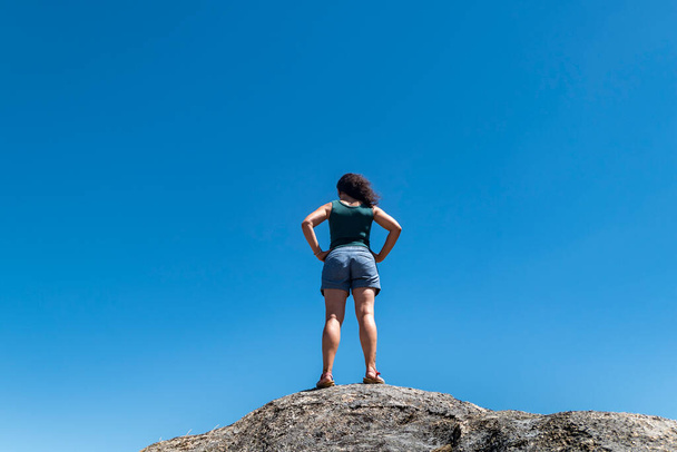 Turystka na szczycie skały odpoczywa ciesząc się widokami wokół niej - Zdjęcie, obraz