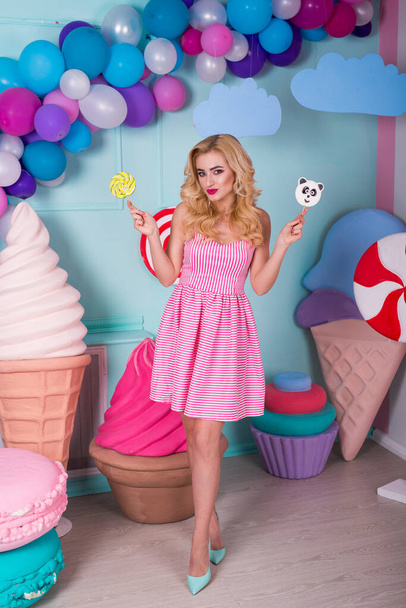 Portrait of amazing sweet-tooth woman in pink dress holding candies and posing on background decorated with huge ice cream. Lollipop panda - Foto, afbeelding