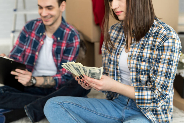 Young couple counting money while sitting on floor in new apartment - Foto, imagen