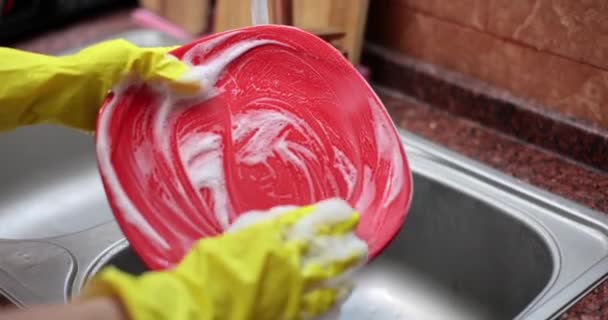 Mãos femininas em luvas de borracha protetoras amarelas lavar placa vermelha. Regras para lavar pratos domésticos - Filmagem, Vídeo