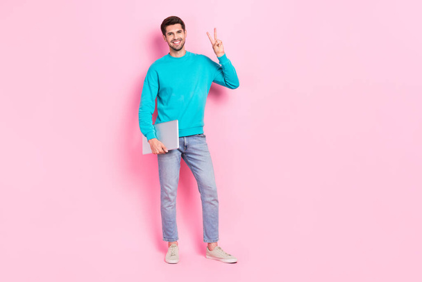 Full body photo of handsome young guy holding laptop entrepreneur showing v-sign wear trendy blue clothes isolated on pink color background. - Fotó, kép