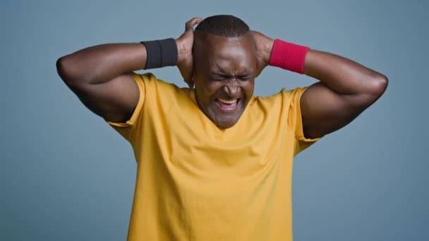 Close-up volwassen mannelijke atleet sportman staan in de studio op grijze achtergrond boos geïrriteerde angstige man die lijdt aan luid lawaai bedekken oren met handen weigeren te luisteren schreeuwen gevoel hoofdpijn - Video