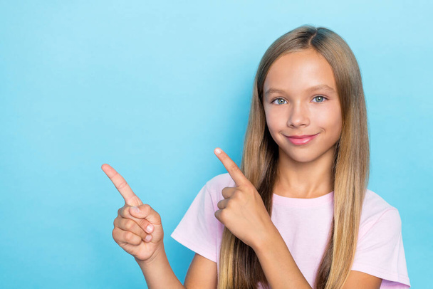 Portrait of good mood small girl straight hairstyle wear pink t-shirt fingers indicating empty space isolated on blue color background. - Zdjęcie, obraz