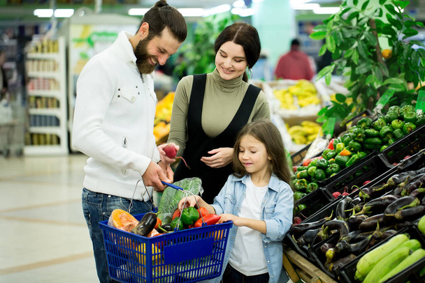 a woman with a man and a child, choosing vegetables while shopping in a vegetable supermarket - Foto, Imagen