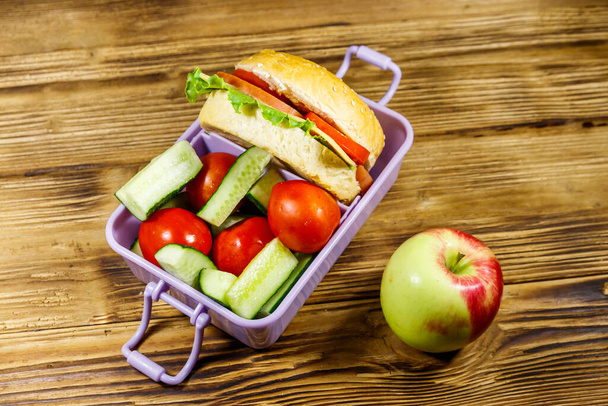 Apple and lunch box with burgers and fresh vegetables on a wooden table - Photo, Image
