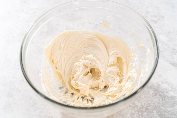 Mezclar los ingredientes con una batidora manual en un tazón grande para hacer glaseado de queso crema para pastel de paquete de zanahoria. - Foto, imagen