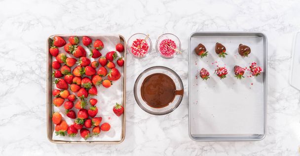 Acostado. Sumergiendo fresas en el chocolate derretido para preparar fresas cubiertas de chocolate. - Foto, imagen