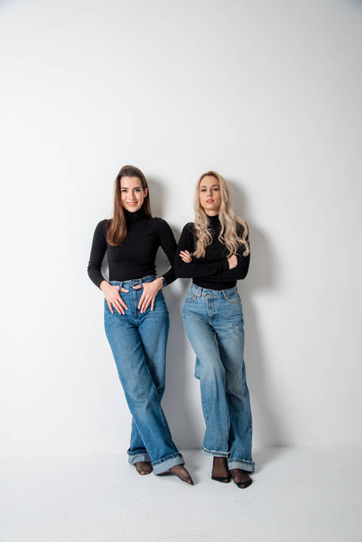 two beautiful girls brunette and blonde posing in studio against gray - Fotoğraf, Görsel