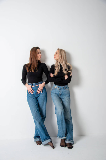 two beautiful girls brunette and blonde posing in studio against gray - Fotó, kép