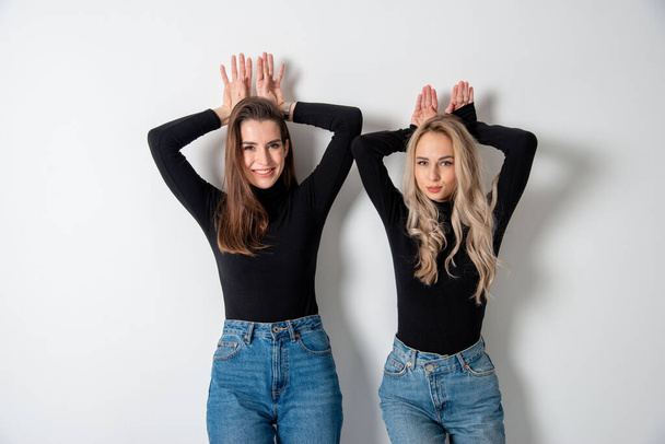 twee mooie meisjes brunette en blond poseren in studio tegen grijs - Foto, afbeelding