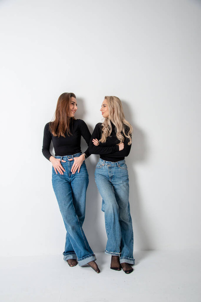 two beautiful girls brunette and blonde posing in studio against gray - Valokuva, kuva