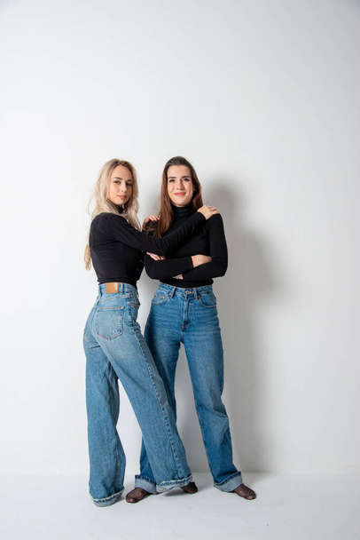 two beautiful girls brunette and blonde posing in studio against gray - Foto, Imagen