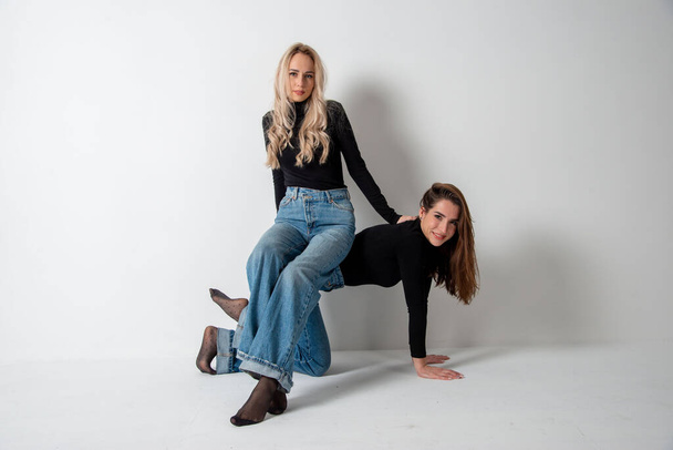 two beautiful girls brunette and blonde posing in studio against gray - Фото, изображение