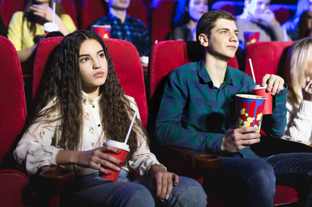 Friends sit and eat popcorn together while watching movies in a movie theater - Fotoğraf, Görsel