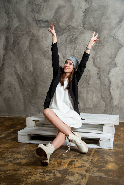 beautiful young woman posing in studio wearing white dress, black jacket and gray hat - Fotoğraf, Görsel