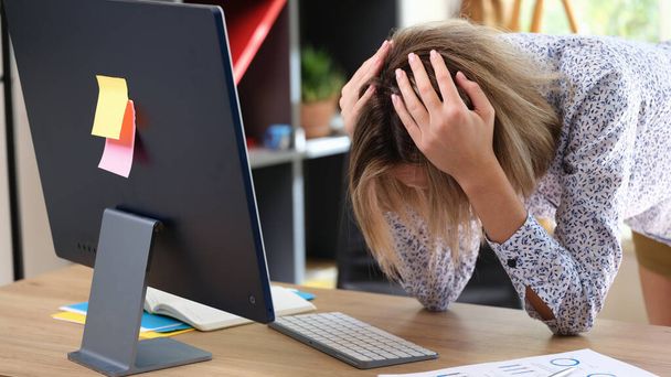 職場でのミスや問題により、従業員は苦しんでいます。女性取得彼女の頭とともに彼女の手でコンピュータの前にテーブルの上. - 写真・画像